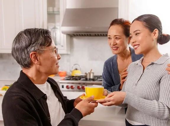 在一個現代化的廚房裏,一家三口望着彼此微笑,同時女兒將一杯飲品遞給父親。