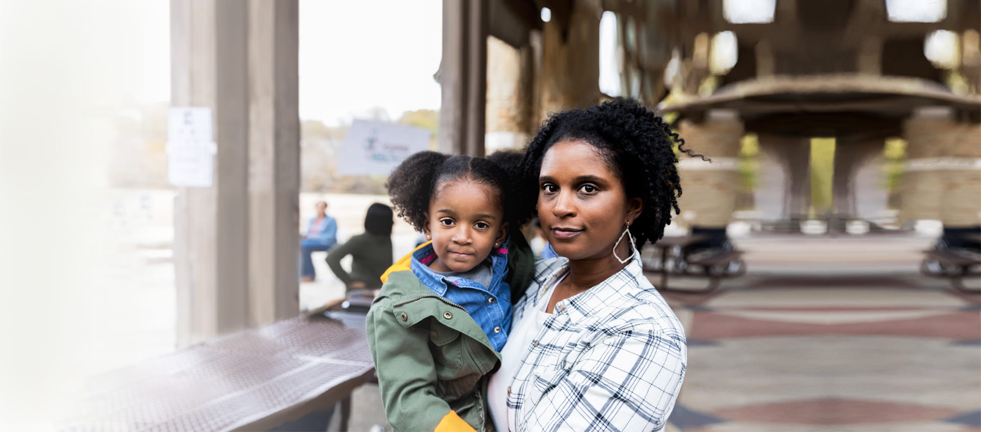 Une mère tient sa fille dans ses bras et toutes deux regardent l’objectif.
