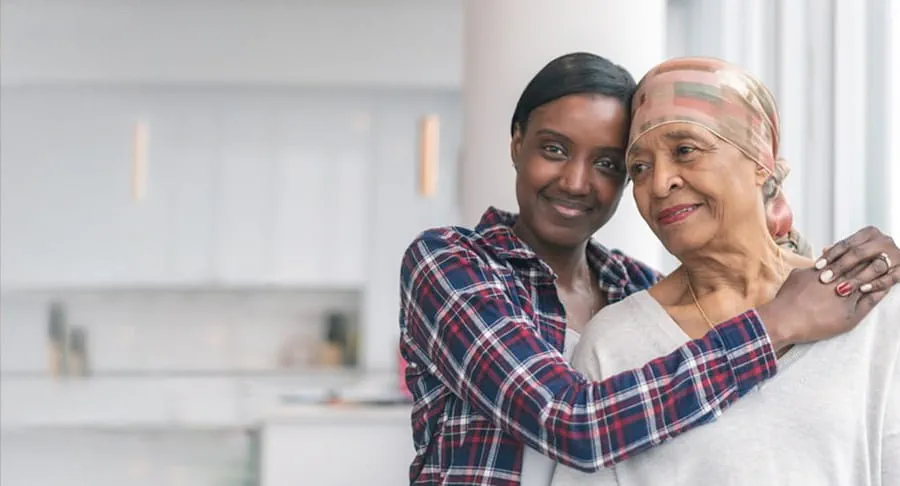 A smiling woman wraps her arms around the shoulders of an older woman