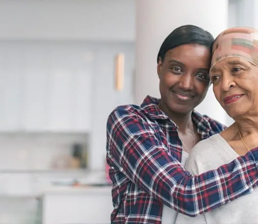 A smiling woman wraps her arms around the shoulders of an older woman