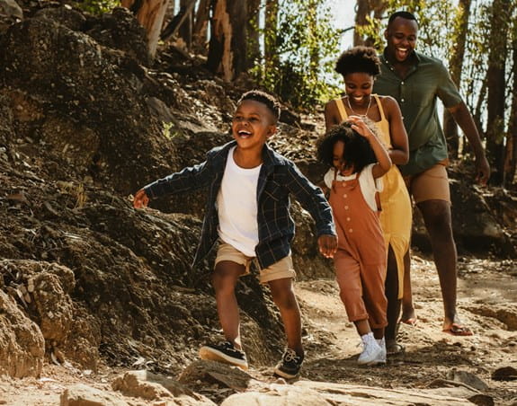 Children running in front of their parents on a trail in the woods.