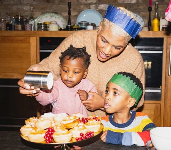 A mother with her two young children decorating cookies in the kitchen.