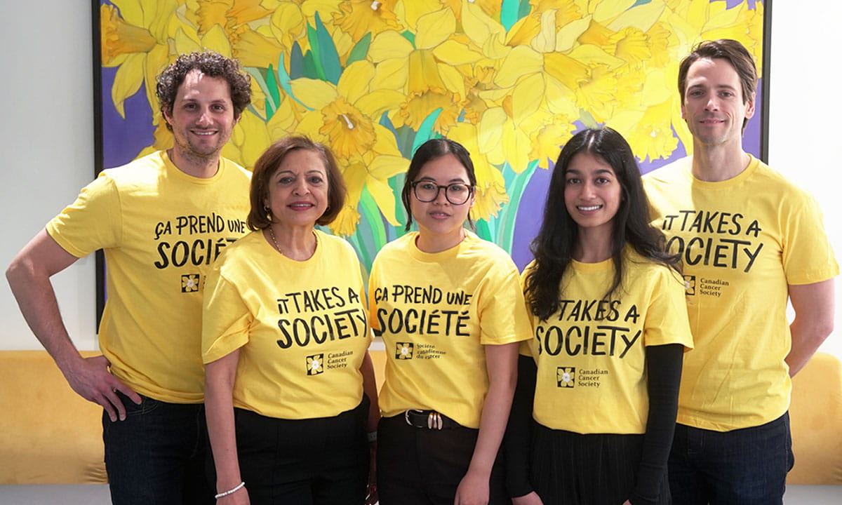 A group of five people wearing matching yellow “It Takes a Society” / « Ça prend une société » shirts pose together.