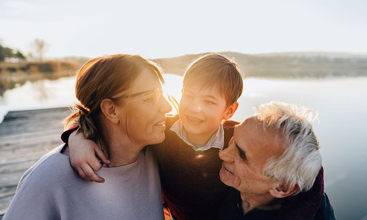 Grandparents and grandchild together by a lakeside dock at sunset.