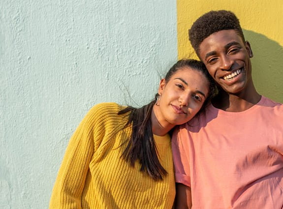 Un jeune homme et une jeune femme se tenant côte à côte devant un mur coloré.