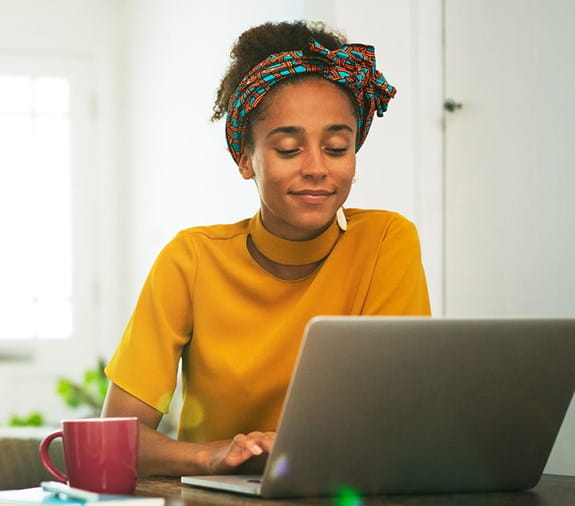 Une jeune femme souriant, assise devant son ordinateur portable.