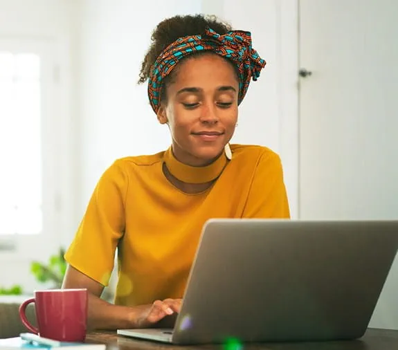 A young woman sits at her laptop smiling.