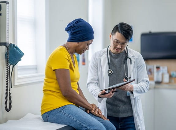 Une femme assise sur une table d’examen, lisant les résultats sur la tablette du médecin.