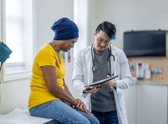 Une femme assise sur une table d’examen, lisant les résultats sur la tablette du médecin.