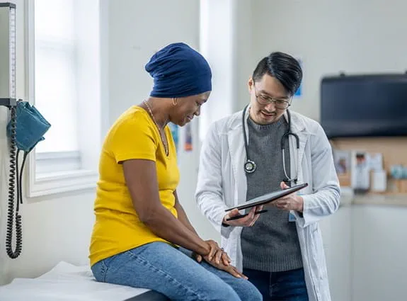 A woman sits on an exam table reading over results with the doctor.