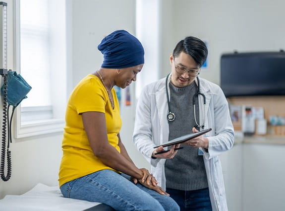 A woman sits on an exam table reading over results with the doctor.