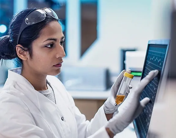 A researcher holds a test tube while touching a touch screen computer.