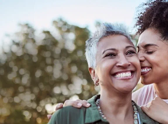 Une mère et sa fille souriant, se serrant dans les bras. La fille presse son visage contre celui de sa mère.
