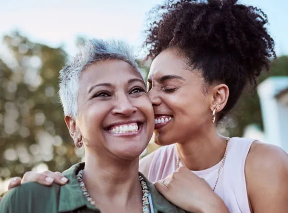 Une mère et sa fille souriant, se serrant dans les bras. La fille presse son visage contre celui de sa mère.
