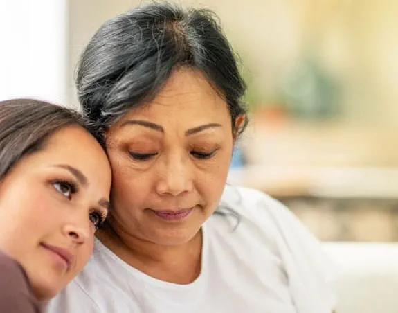 A mother and daughter sitting on a couch with their faces pressed against each other.